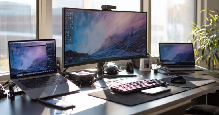 Laptop dock station connected to dual monitors with mechanical keyboard and cooling pad on desk