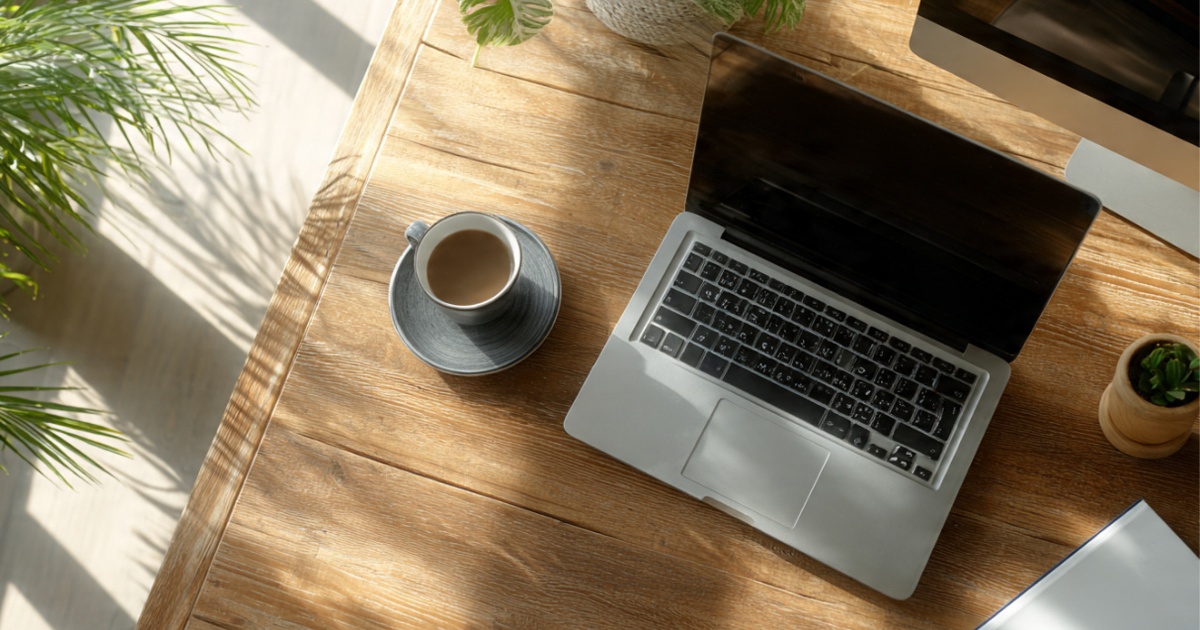 Remote worker using laptop with external monitor in bright home office with coffee and notebook